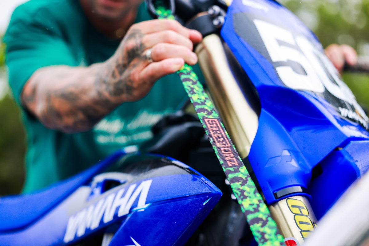 Rider tightening a Green Camo Strap Onz strap on a dirt bike