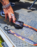 Hand pressing the release on a Strap Onz Retractable Flames strap on a checker-plate ute tray, coated S-hook in view