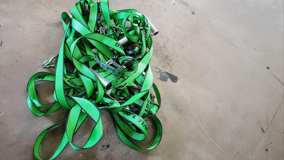 Tangled pile of green standard ratchet straps on concrete